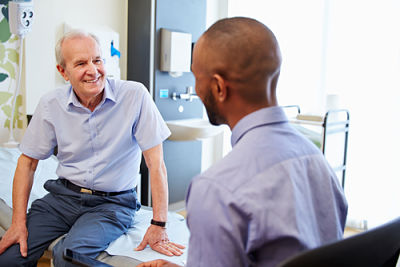 An elder man is smiling and conversing with a younger man