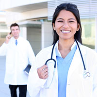 A smiling female nurse and a smiling male nurse in the background holding a cell phone